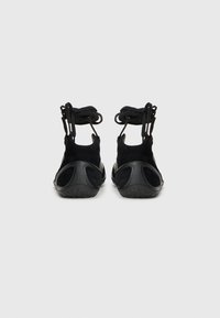 Chaussures en suède noir et caoutchouc avec une forme arrondie, dotées d'une semelle texturée et d'un laçage à l'arrière. Le design à talon ouvert améliore la respirabilité.