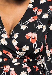 Robe portefeuille florale en tissu noir ornée de motifs de tulipes roses, blanches et rouges. Décolleté en V, taille ajustée et texture douce.