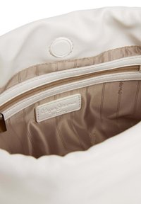 Keskikokoinen valkoinen keinonahkainen laukku, jonka sisäpuolella on beige raidallinen vuori, vetoketjutasku ja näkyvissä oleva merkkilappu.