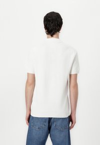 Vit kortärmad stickad tröja med texturerad yta, med rund halsringning och ribbad nederdel, tillsammans med blå denimjeans.