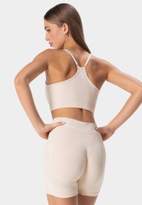 Sujetador deportivo beige con tirantes ajustables y un logo en la parte posterior, combinado con shorts de talle alto a juego que presentan acentos moldeadores.