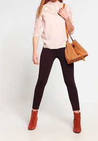 Světle růžová krajková blůza s tříčtvrtečními rukávy, spojená s tmavě fialovými legínami. Hnědá semišová kabelka a odpovídající kotníkové boty.