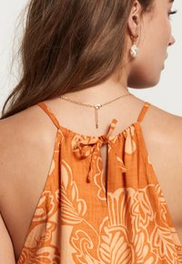 Top halter floral naranja con tirantes finos, que presenta un detalle de lazo en la parte posterior y un acento decorativo de cadena cerca del escote.