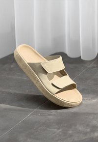 Sandal de slide bege com duas correias ajustáveis, sola de borracha texturizada e material superior macio. Design minimalista com a ponta arredondada.