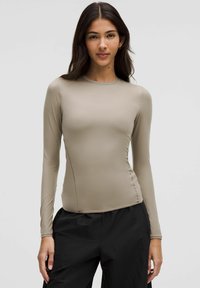 Dugih rukava, uski top u bež boji, izrađen od glatkog, rastezljivog materijala. Ima okrugli izrez i minimalne šavove za elegantan izgled.