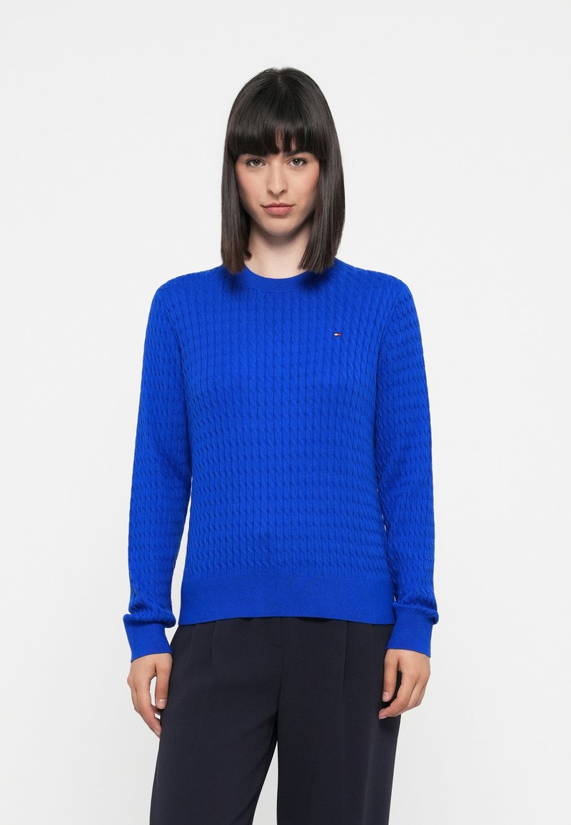 Pull en maille bleu avec un motif texturé, col rond et poignets côtelés. Présente un petit logo en accent sur la poitrine.