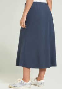 Granatowa spódnica sięgająca kostek, wykonana z miękkiego, gładkiego materiału. Posiada ukryty pas i luźny krój, zestawiona z srebrnymi tenisówkami.
