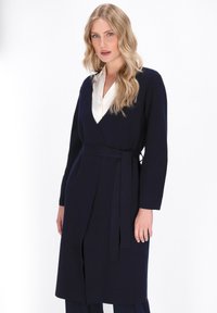 Marineblaue Wickelkleid mit langen Ärmeln, V-Ausschnitt und Gürtel. Weicher Stoff mit glatter Textur. Elegantes und minimales Design.