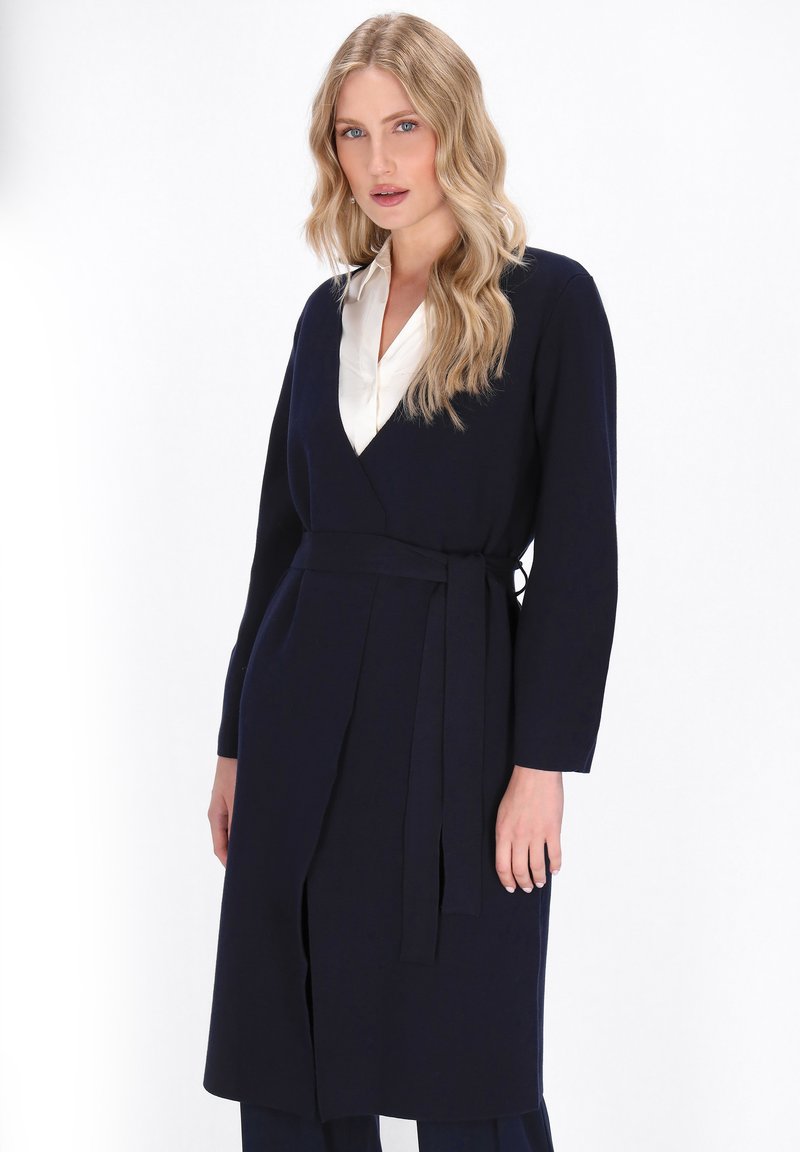 Marineblaue Wickelkleid mit langen Ärmeln, V-Ausschnitt und Gürtel. Weicher Stoff mit glatter Textur. Elegantes und minimales Design.