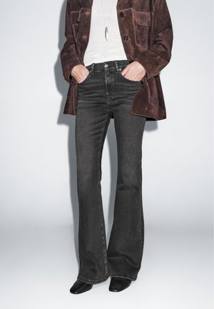 Dark gray flared jeans with a high waist, paired with a brown suede jacket and black pointed ankle boots. Simple, textured, and fitted design.