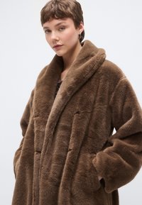 Bruine mantel van zachte imitatiebont met een brede kraag, oversized pasvorm en zijzakken. Heeft een zachte textuur en een gladde, warme uitstraling.