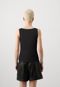 Svart ermeløs topp med ribbestruktur og kontrastfarget hvit sikksakk-søm langs rundt halsen og armehullene. Kombinert med svarte skinnshorts.