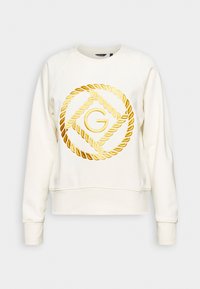 Krämfärgad sweatshirt med ett stort guldbroderat emblem med en cirkulär repdesign och bokstaven "G" i centrum. Ribbad mudd.