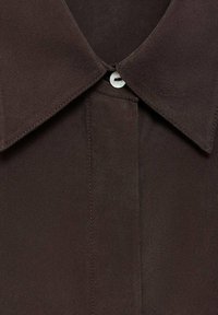 Camicia marrone con bottoni, dotata di un ampio colletto, chiusura con un singolo bottone e una texture di tessuto liscia. Presenta cuciture pulite lungo le cuciture.