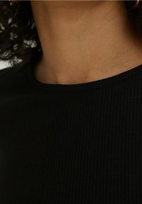 Czarny prążkowany top z okrągłym dekoltem i miękką fakturą. Tkanina wydaje się elastyczna, przylegająca do ciała.