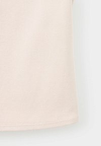 Gros plan d’un tissu côtelé beige montrant la texture et l’ourlet cousu d’un vêtement.