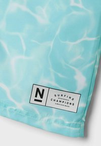 Lichtblauwe zwemshorts met een watertextuurpatroon, met een zwart label met witte tekst en logo in de rechteronderhoek.