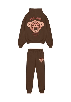 Bruine hoodie- en joggingbroekset met een roze afbeelding van een abstracte apengezicht en tekst op de achterkant van de hoodie en de voorkant van de broek.