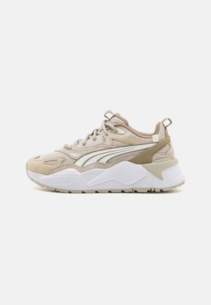 Chaussure de sport beige avec des matériaux en maille et en daim, bout arrondi, semelle blanche texturée et une bande latérale proéminente avec des accents crème et beige.