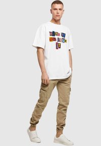 Hvid T-shirt med korte ærmer og multicolor blokbogstaver, der står "HATE IT OR LOVE IT"; parret med beige cargo bukser og hvide sneakers.