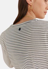 Stripet bomulds T-shirt i hvid og navy, med rund halsudskæring og en lille logo detalje på ryggen, korte ærmer og en afslappet pasform.