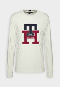 Koszulka z długim rękawem w kolorze kremowym z dużym, haftowanym logo w granatowym i czerwonym kolorze z napisem "TOMMY HILFIGER" na środku. Miękka w dotyku.