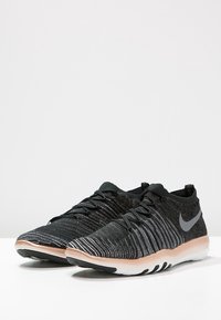 Scarpe sportive nere con una parte superiore testurizzata, caratterizzate da un motivo sfumato, dettagli grigi e una suola di un beige chiaro. Design con lacci per una vestibilità aderente.