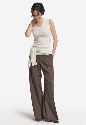Top in cotone bianco a coste con un maglione leggero annodato in vita, abbinato a pantaloni marroni a gamba larga con un tessuto strutturato.