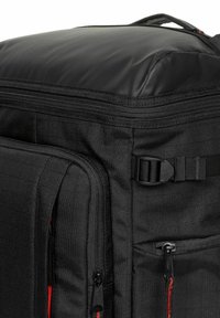 Black backpack with textured fabric, multiple zippered compartments, a padded top, and an adjustable strap. Red accents on zippers.