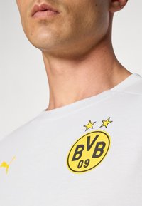 Hvid T-shirt med gul BVB-logo med to stjerner og sort skrift. Blødt stof, rund hals-design og lille Puma-logo på ærmet.