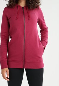 Tmavě červená mikina na zip s kapucí, dlouhými rukávy, předními kapsami a žebrovanými manžetami. Hladký materiál a šňůrky na kapuci.