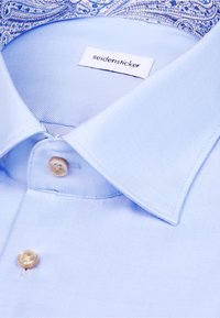 Chemise bleu clair à texture lisse, dotée d'une fermeture à boutons et d'un col à motifs. L'étiquette indique "seidensticker".
