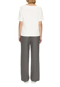 Vit t-shirt med kort ärm och vid halsringning, tillsammans med grå vida byxor och vita sneakers. Slät tyg, avslappnad passform.