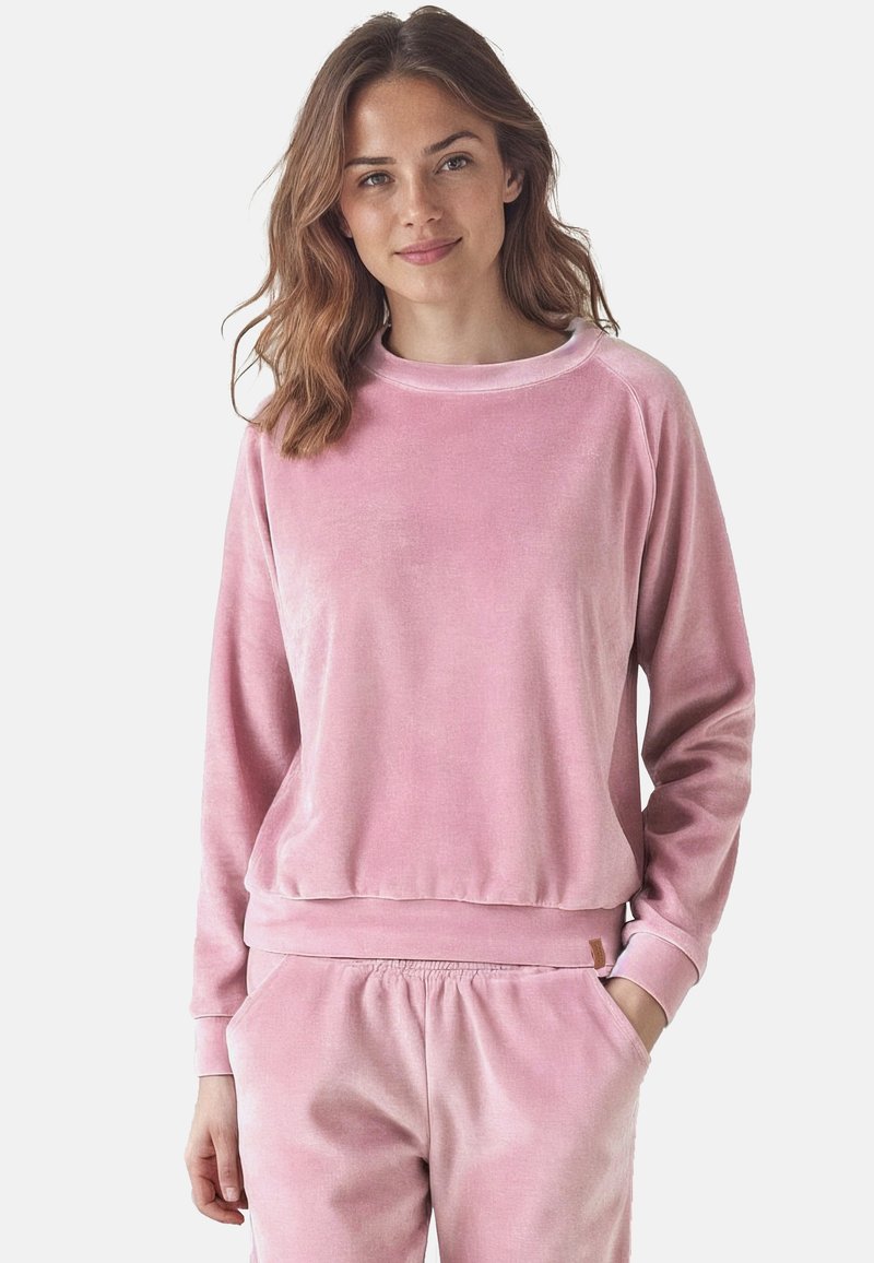 Felpa in velluto rosa con una vestibilità rilassata, scollo rotondo e polsini e orlo a coste. Texture liscia con una leggera lucentezza. Abbinata a pantaloni rosa coordinati.