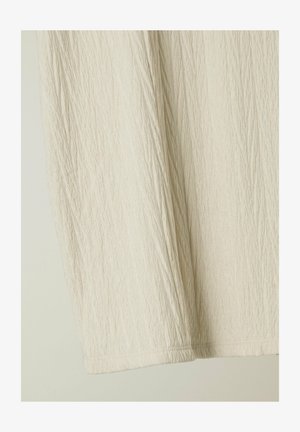 Vaalea beige kangas, jossa on teksturoitu, rypistyneet pinta. Vaate on yksinkertainen, ilman koristeita ja siinä on pehmeä, hieman löysä istuvuus.