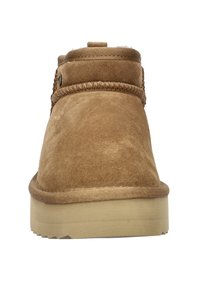 Tan suède enkellaars met een ronde neus, decoratieve stiksels en een platte rubberen zool. Heeft een gestructureerde afwerking en een klein logo-accent.