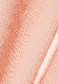 Tissu de couleur pêche douce avec un motif tricoté finement texturé et de légers plis créant des ombres douces.