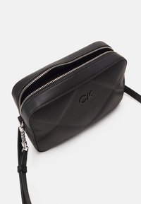 Czarna pikowana skórzana torba na ramię z srebrnymi akcentami, podwójnymi zamkami błyskawicznymi i wytłoczonym logo z przodu. W zestawie regulowany pasek.