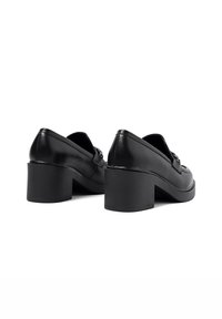 Scarpe platform in pelle nera con punta arrotondata, scollatura bassa e tacco spesso. Presentano un accento decorativo sulla parte anteriore.