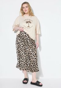 Crème oversized t-shirt met palmbomenprint, gecombineerd met een lange rok in luipaardprint. Zwarte platte sandalen maken de outfit compleet.
