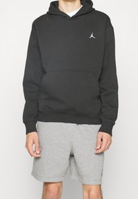 Felpa nera con cappuccio, tasca a marsupio, polsi e orlo a costine. Presenta un piccolo logo Jumpman bianco sul lato sinistro del petto. Abbinato a pantaloni Corti grigi.