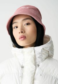 Rosa kordfläcks bucket hat med ribbad textur, kombinerad med en glänsande vit puffjacka med hög krage och detaljer i silvermetall.