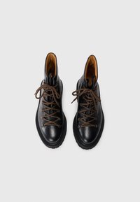 Schwarze Lederstiefel mit braunen Schnürsenkeln, strukturiertem Finish, verstärkter Zehenkappe, gepolstertem Kragen und Gummisohle. Höhe: Knöchel.