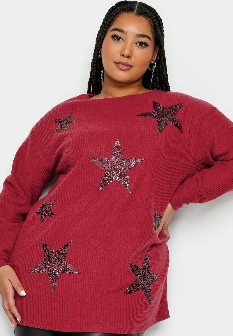 Röd stickad tröja med ribbad textur och oversized passform, med flera mörka paljetter i form av stjärnor som dekorativa detaljer.