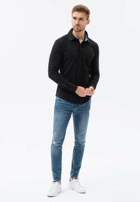 Camicia nera con colletto blu, abbinata a jeans skinny azzurri effetto usurato e sneaker bianche. Tessuto morbido, vestibilità aderente.