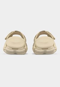 Paire de sandales beige à enfiler avec coussinets et sangles arrière ajustables, vue de face sur un fond blanc uni.