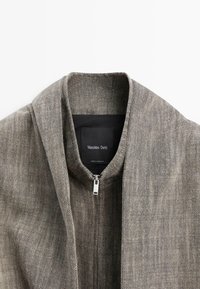 Giacca in tessuto grigio con collo alla coreana e cerniera argentata, etichettata Massimo Dutti, made in Marocco.