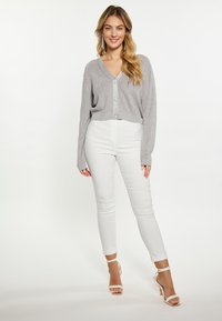 Cardigan corto grigio chiaro con scollatura a V, chiusura con bottoni e trama a costine abbinato a jeans bianchi aderenti e sandali con cinturino.