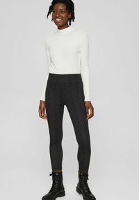 Leggings a quadri neri con vita alta, caratterizzati da una texture liscia e un tessuto elastico. Abbinati a un top bianco a maniche lunghe aderente.