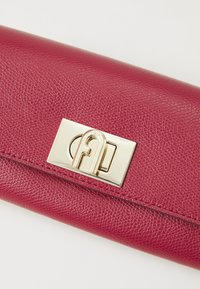 Pochette en cuir fuchsia avec une surface texturée, quincaillerie dorée avec un fermoir logo, et une forme rectangulaire élégante.